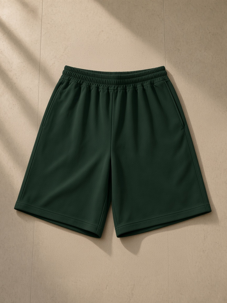 Unisex heavyweight shorts in Blackish Green, laid flat on pale limestone