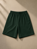 Unisex heavyweight shorts in Blackish Green, laid flat on pale limestone