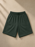 Unisex heavyweight cotton shorts in Dark Green, laid flat on pale limestone