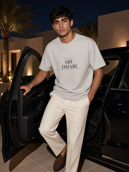Man in the Abu Dhabi Heavyweight Drop Shoulder T-Shirt in Oat Gray stepping out of a car at a desert villa in Abu Dhabi at night