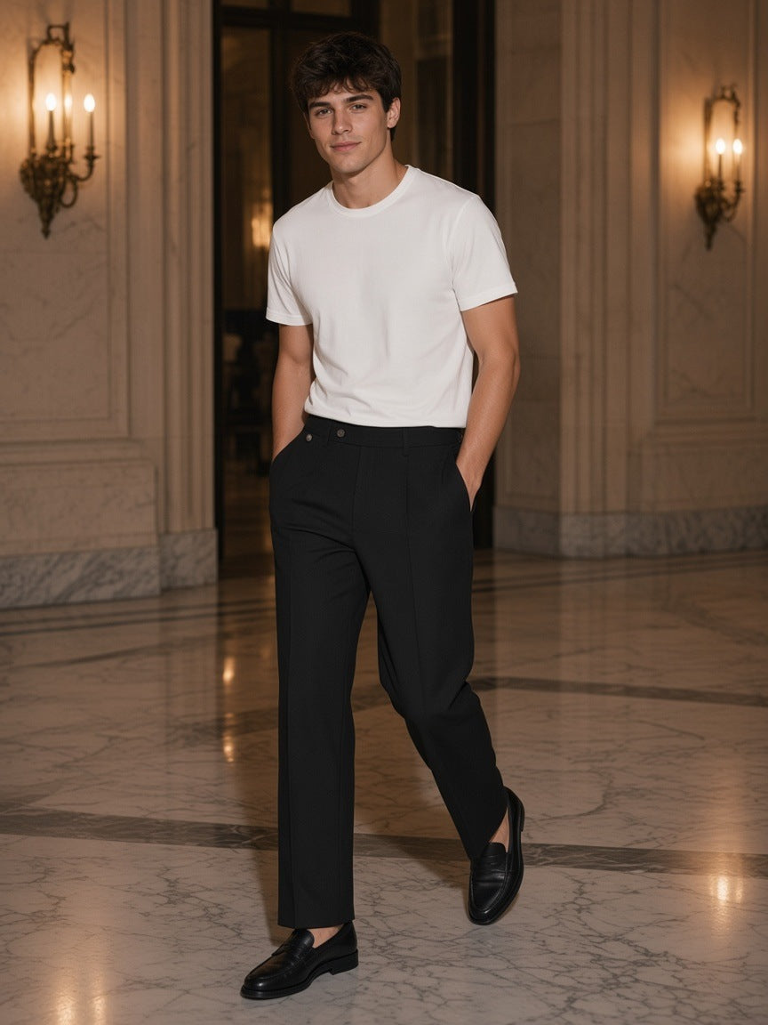 Man in the Adjustable Waist Straight-Leg Pants in Black with a white tee and loafers, walking through a marble hotel lobby at night