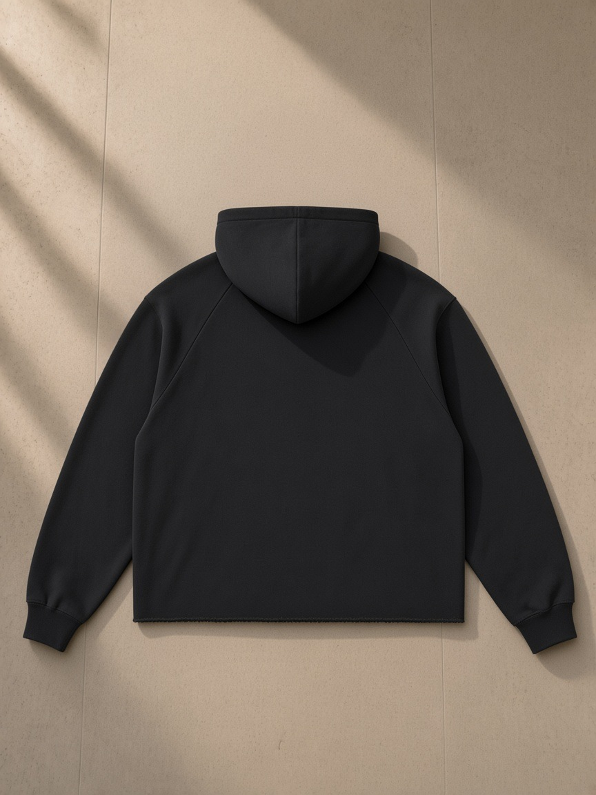 Vintage wash raw edge boxy hoodie in Black, laid flat on pale limestone, back view