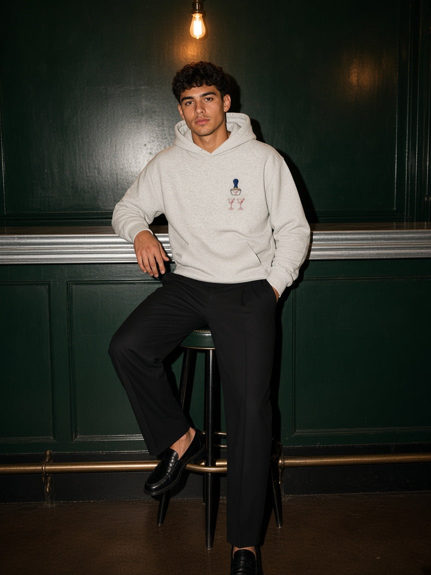 Man in the Bare Bulb hoodie in Oat Gray on a bar stool in a green-panelled bar at night