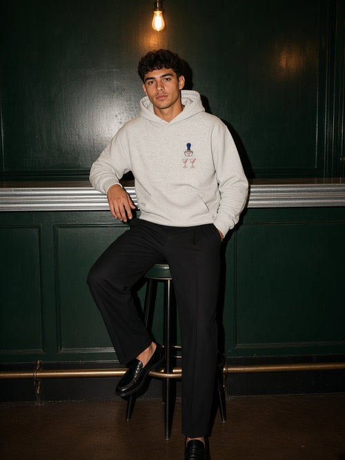 Man in the Bare Bulb hoodie in Oat Gray on a bar stool in a green-panelled bar at night