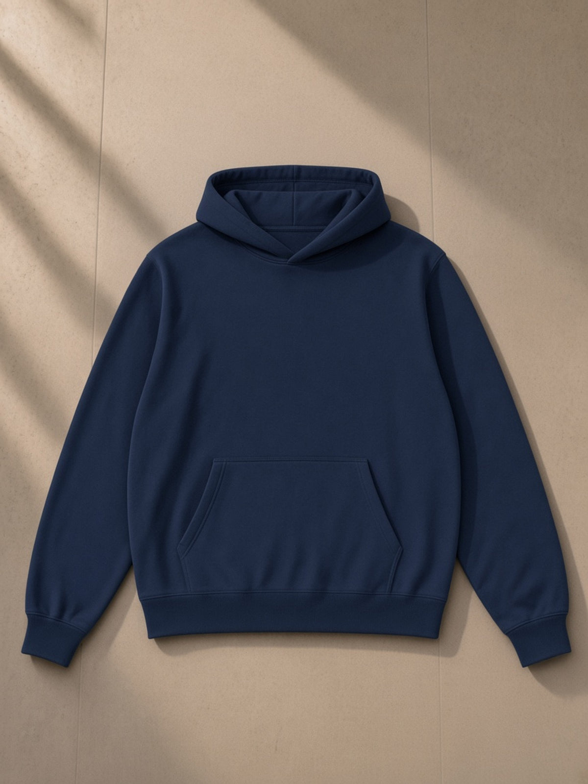 Unisex fleece regular shoulder hoodie in Navy Blue, laid flat on pale limestone, front view