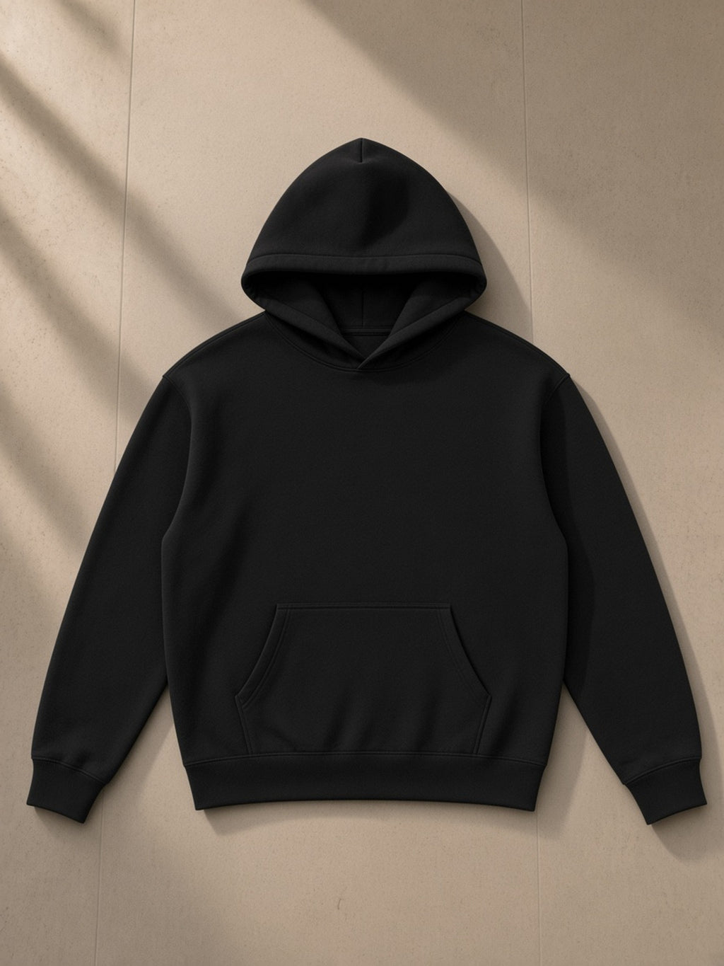 Oversize fleeced hoodie in Black, laid flat on pale limestone