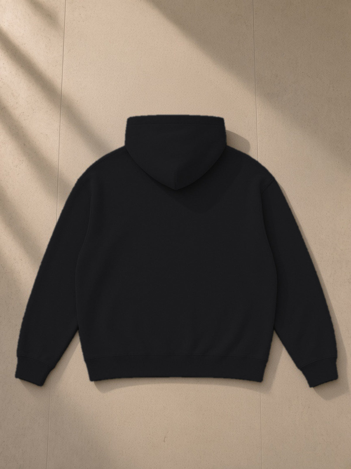 Oversize fleeced hoodie in Black, laid flat on pale limestone, back view