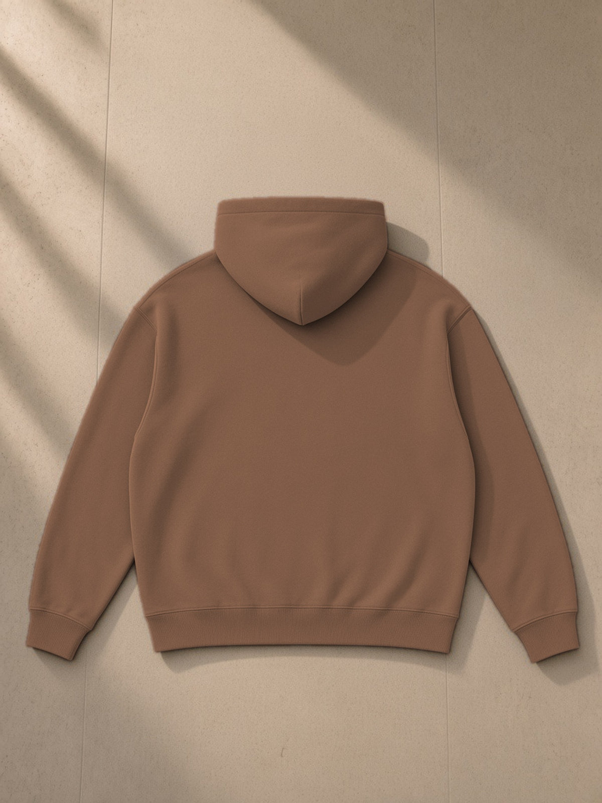 Oversize fleeced hoodie in Brown, laid flat on pale limestone, back view