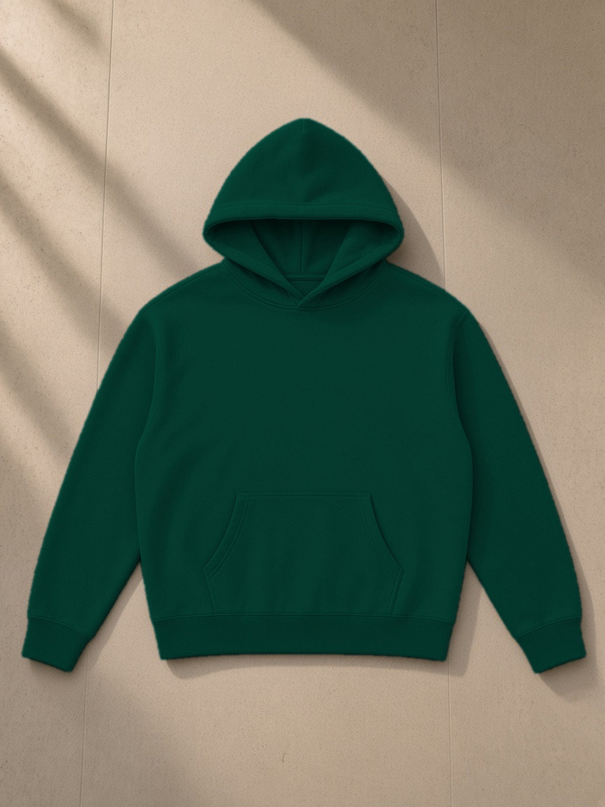 Oversize fleeced hoodie in Eden Green, laid flat on pale limestone