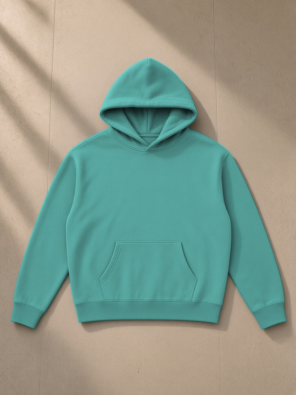 Oversize fleeced hoodie in Medium Green, laid flat on pale limestone