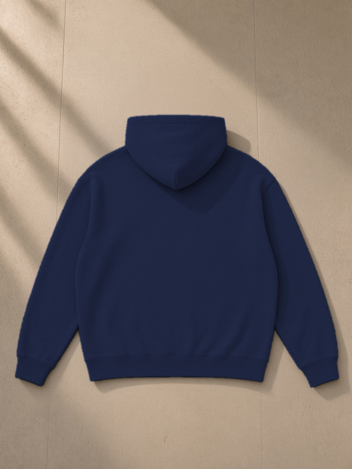 Oversize fleeced hoodie in Navy Blue, laid flat on pale limestone, back view