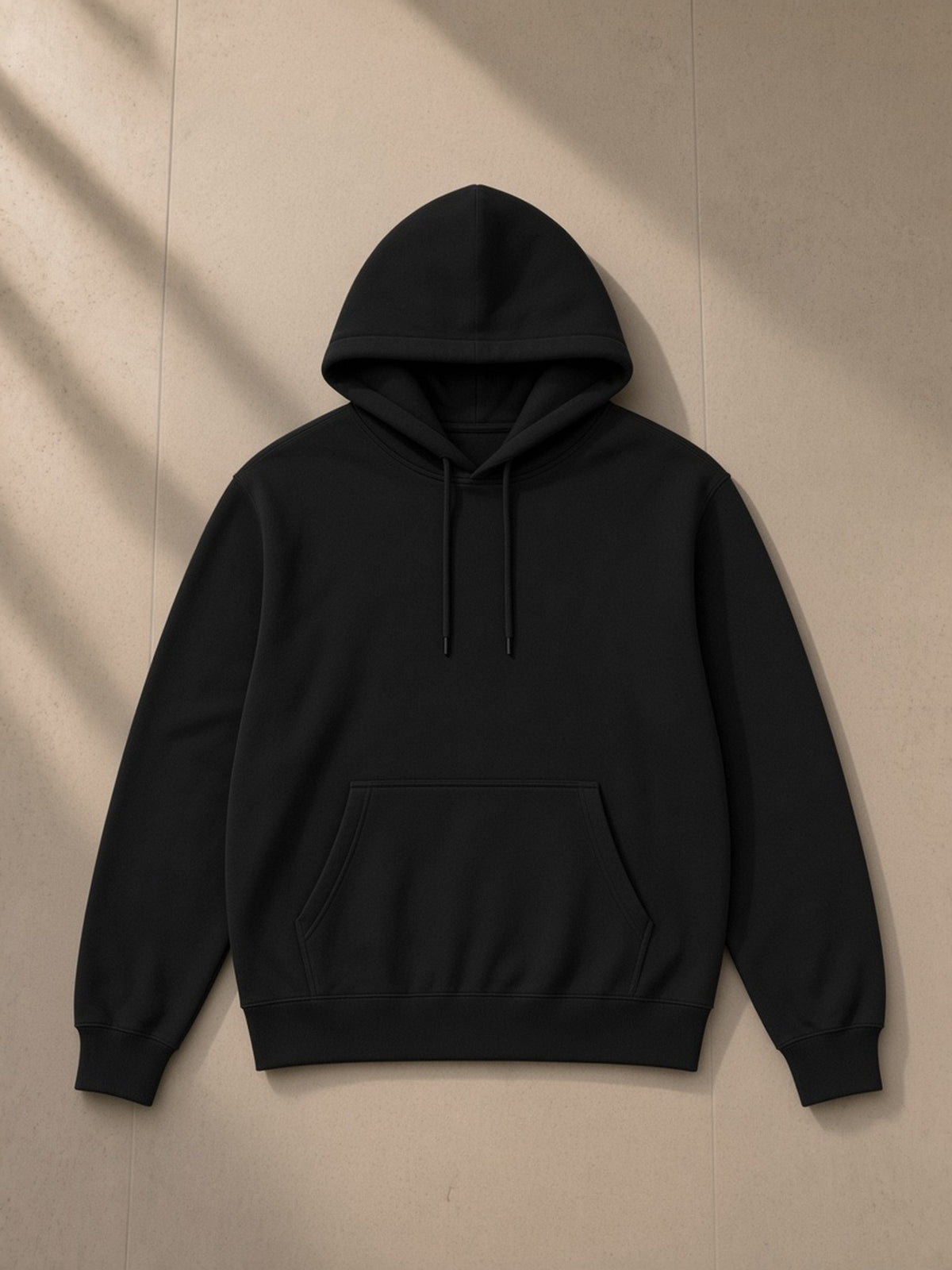 Unisex classic cotton hoodie in Classic Black, laid flat on pale limestone