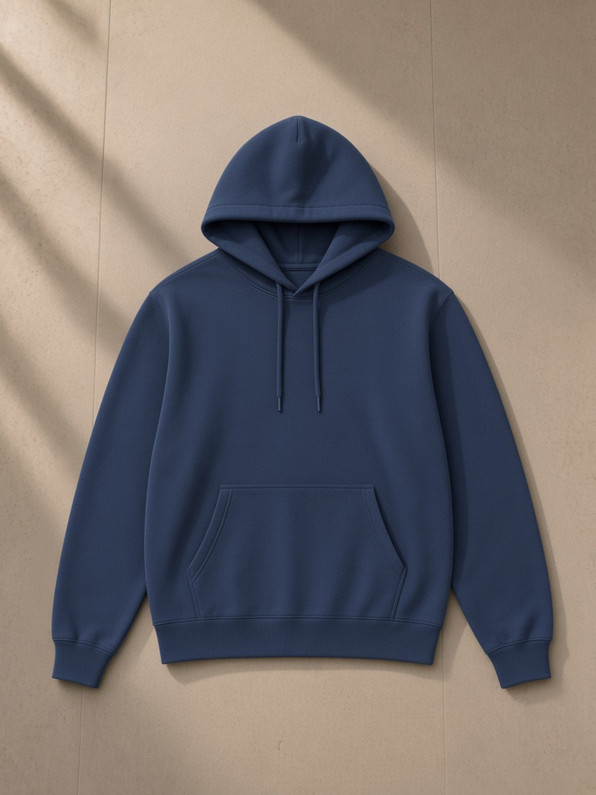 Unisex classic cotton hoodie in Ink Blue, laid flat on pale limestone
