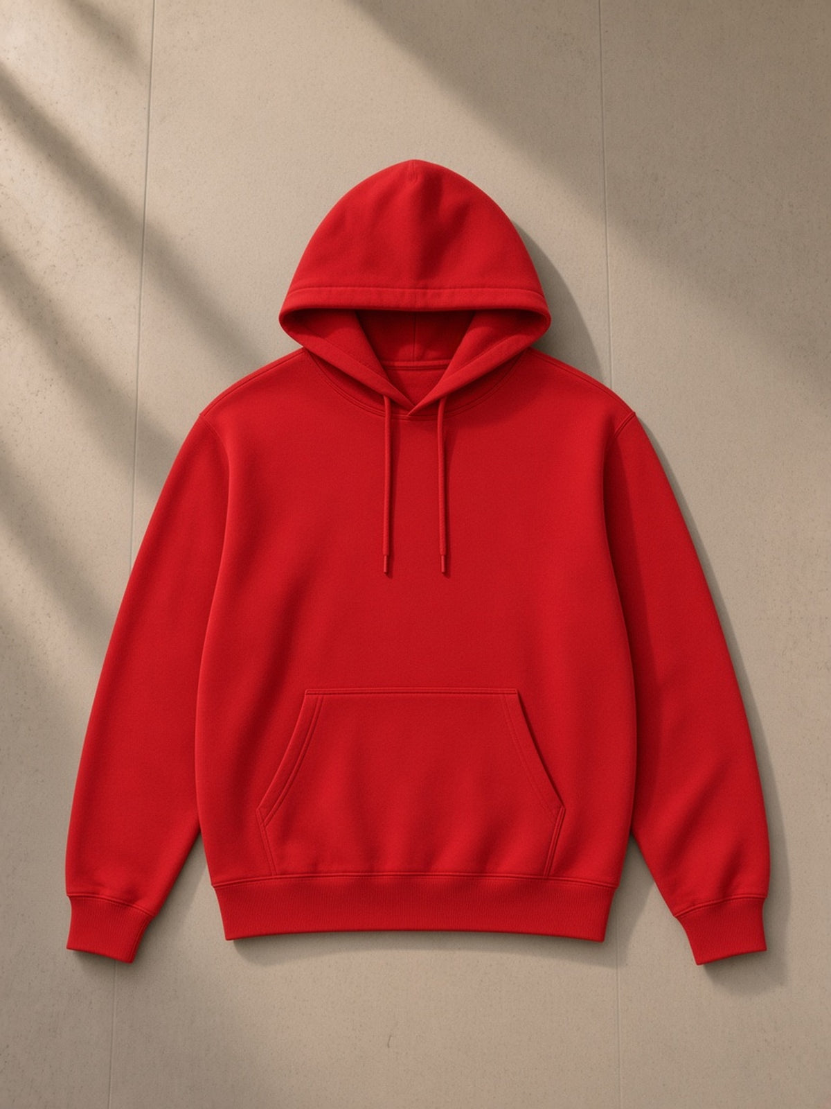 Unisex classic cotton hoodie in Red, laid flat on pale limestone