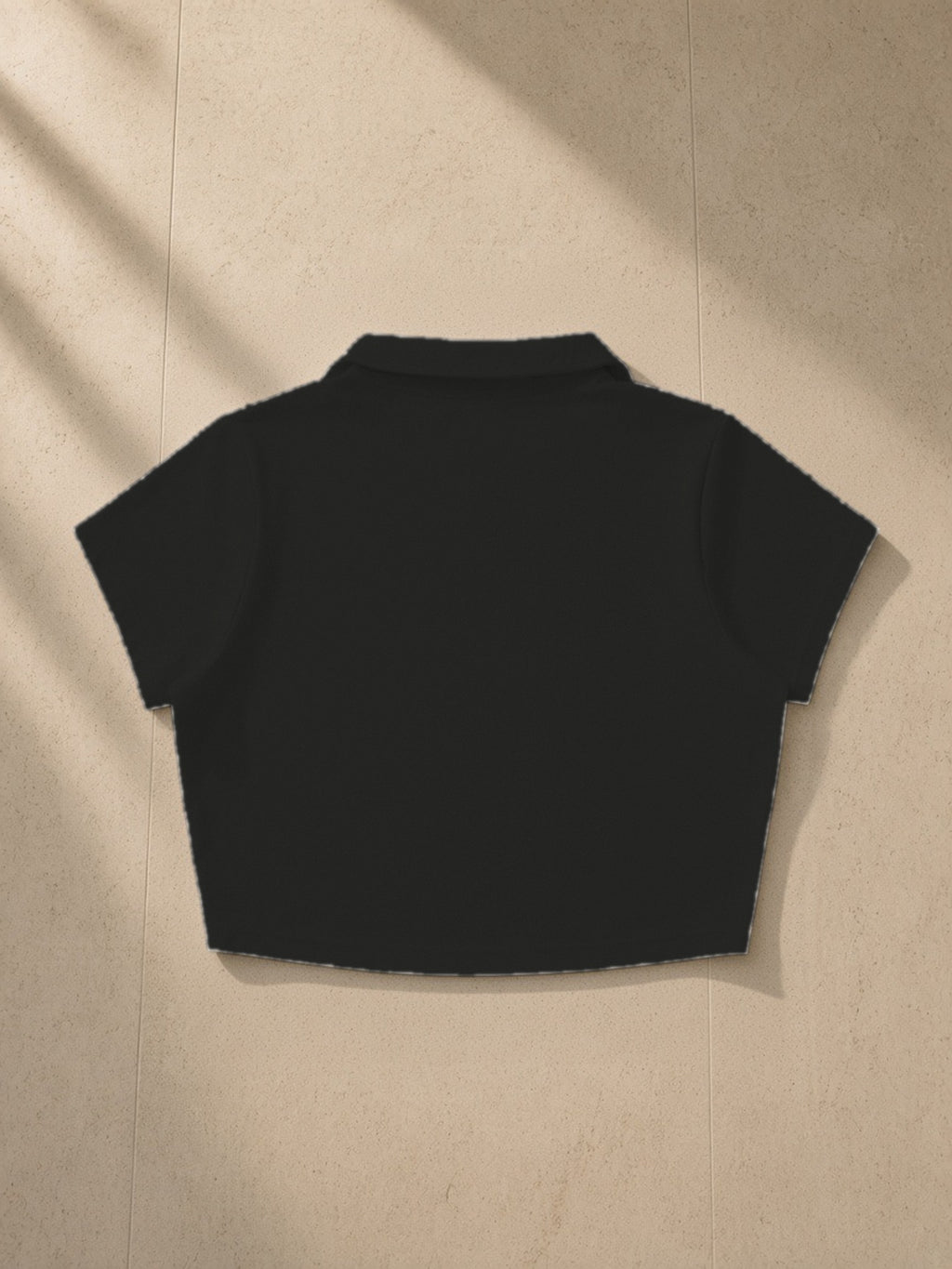 V-Neck Lapel Crop Top in Black, laid flat on pale limestone, back view