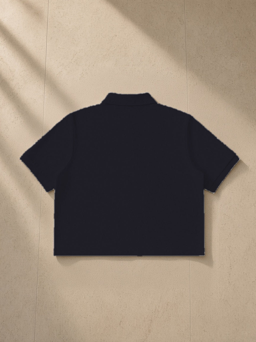 Cropped polo shirt in Black, laid flat on pale limestone, back view