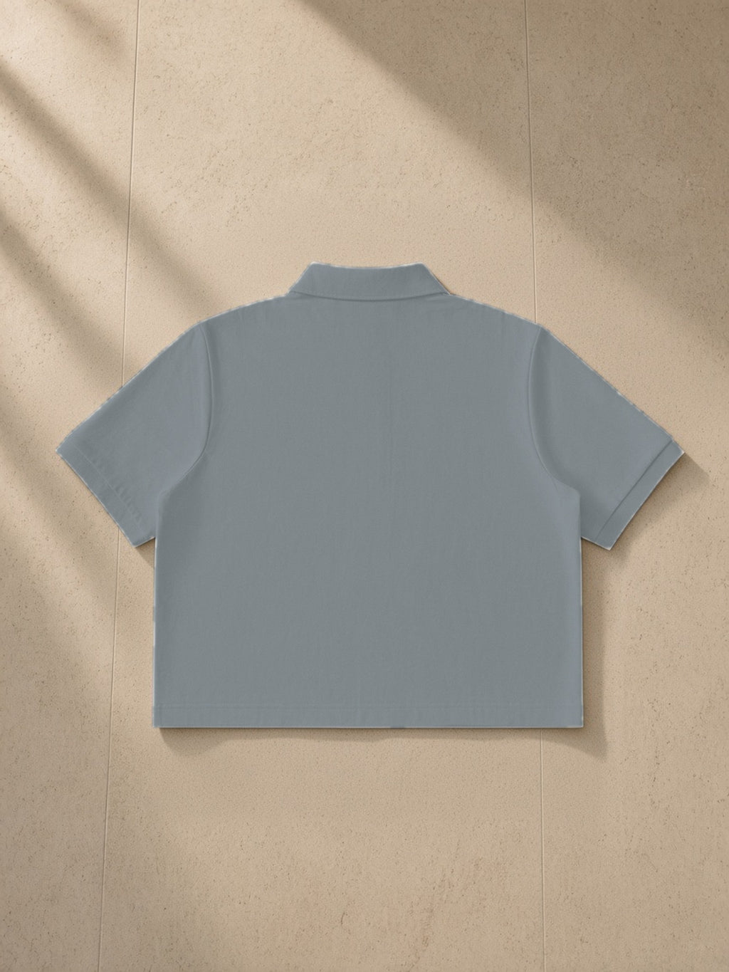 Cropped polo shirt in Gray, laid flat on pale limestone, back view