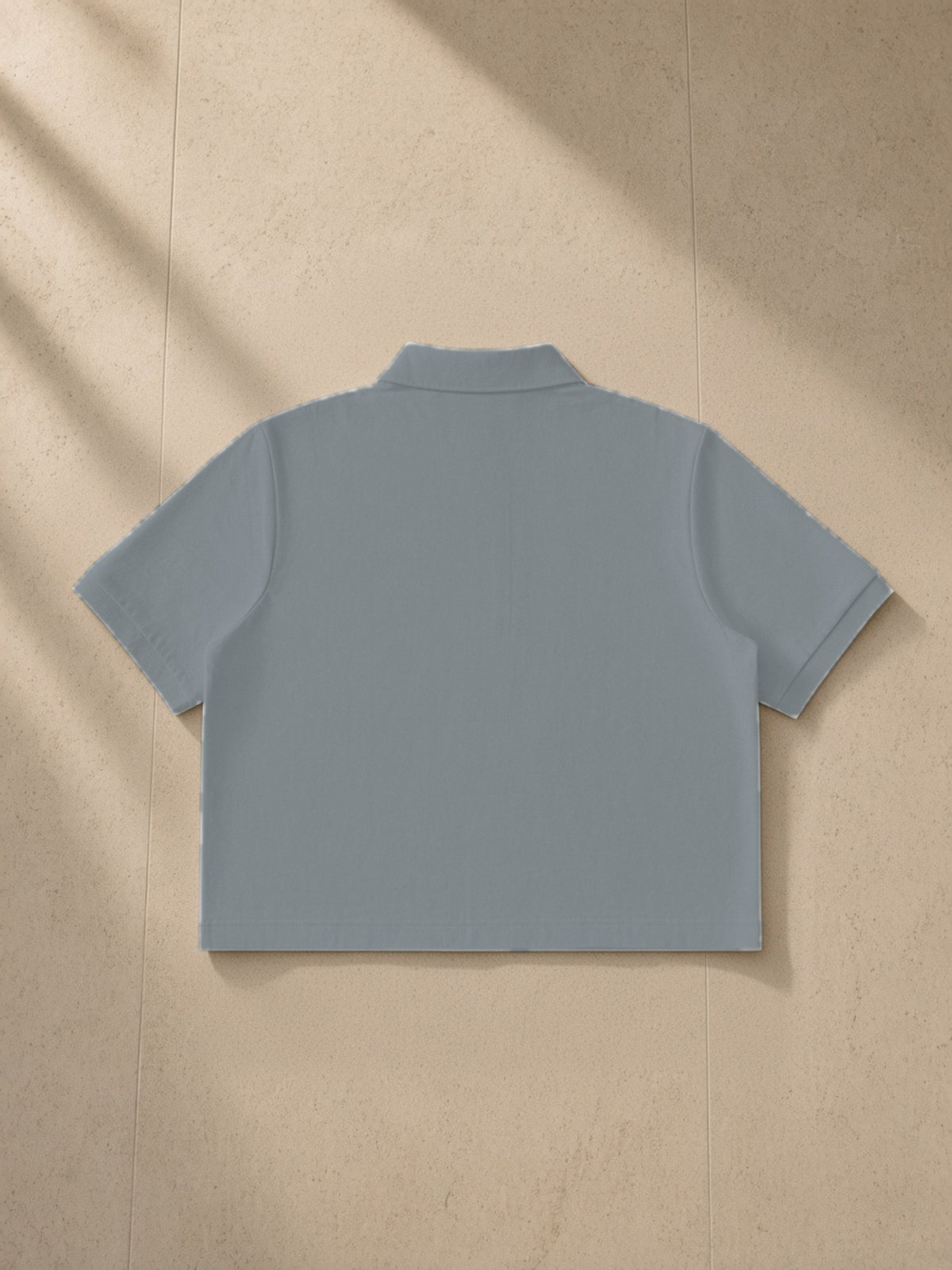 Cropped polo shirt in Gray, laid flat on pale limestone, back view