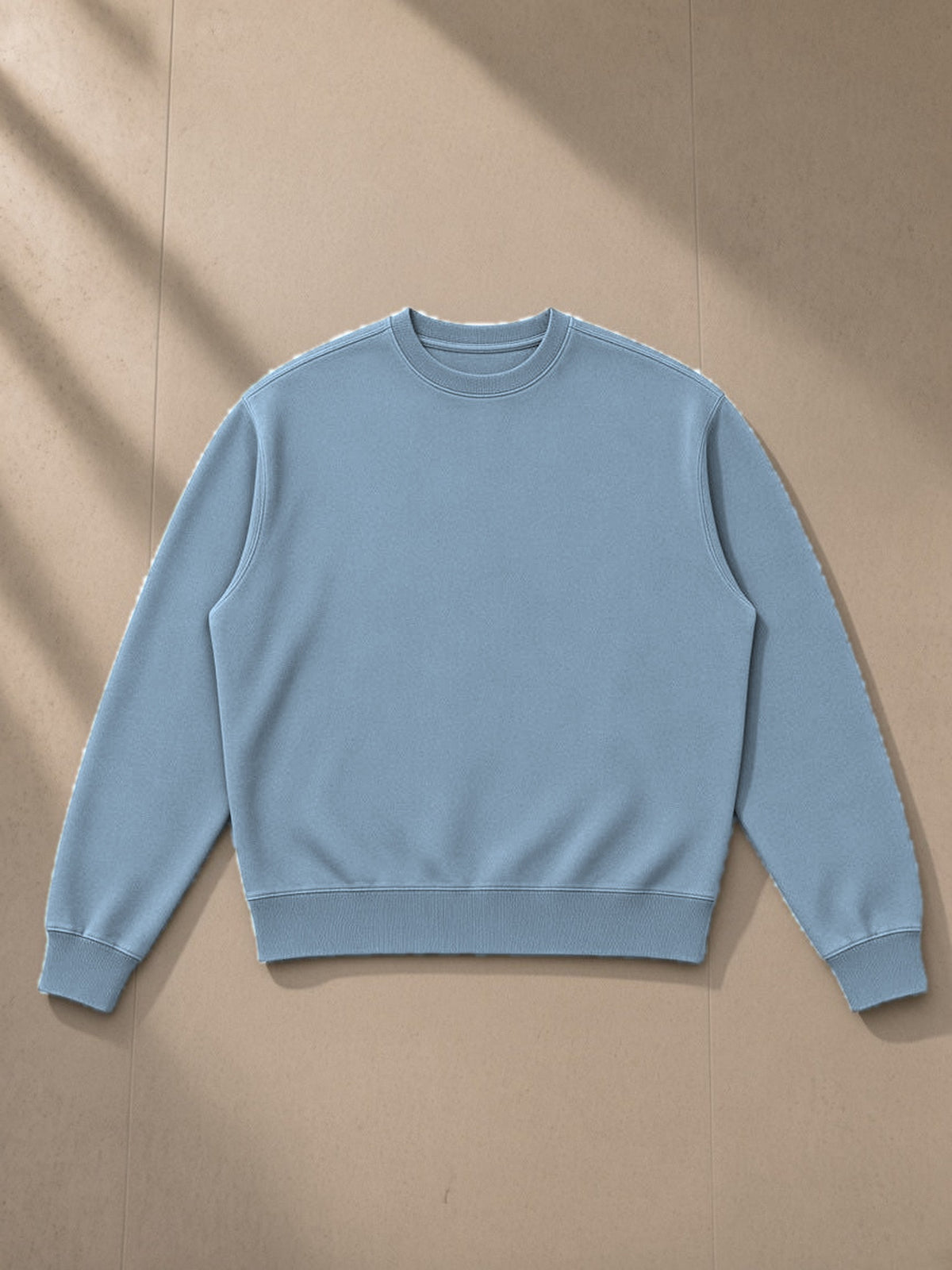 Unisex vintage wash crewneck sweatshirt in Jeans Blue, laid flat on pale limestone, front view