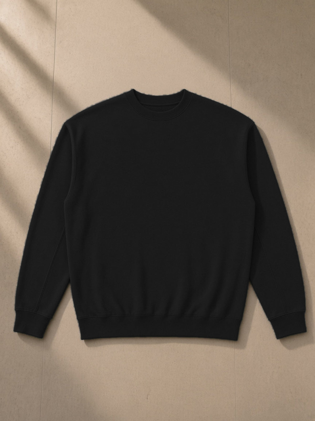 Drop Shoulder Crewneck Sweatshirt in Black, laid flat on pale limestone, front view