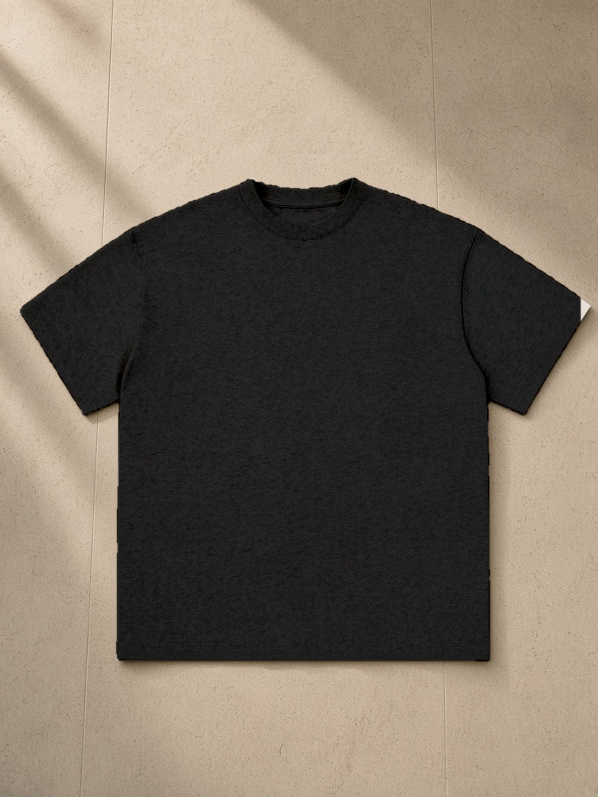 Essential Cotton T-Shirt, 260 gsm, Drop Shoulder in Black, laid flat on pale limestone, front view