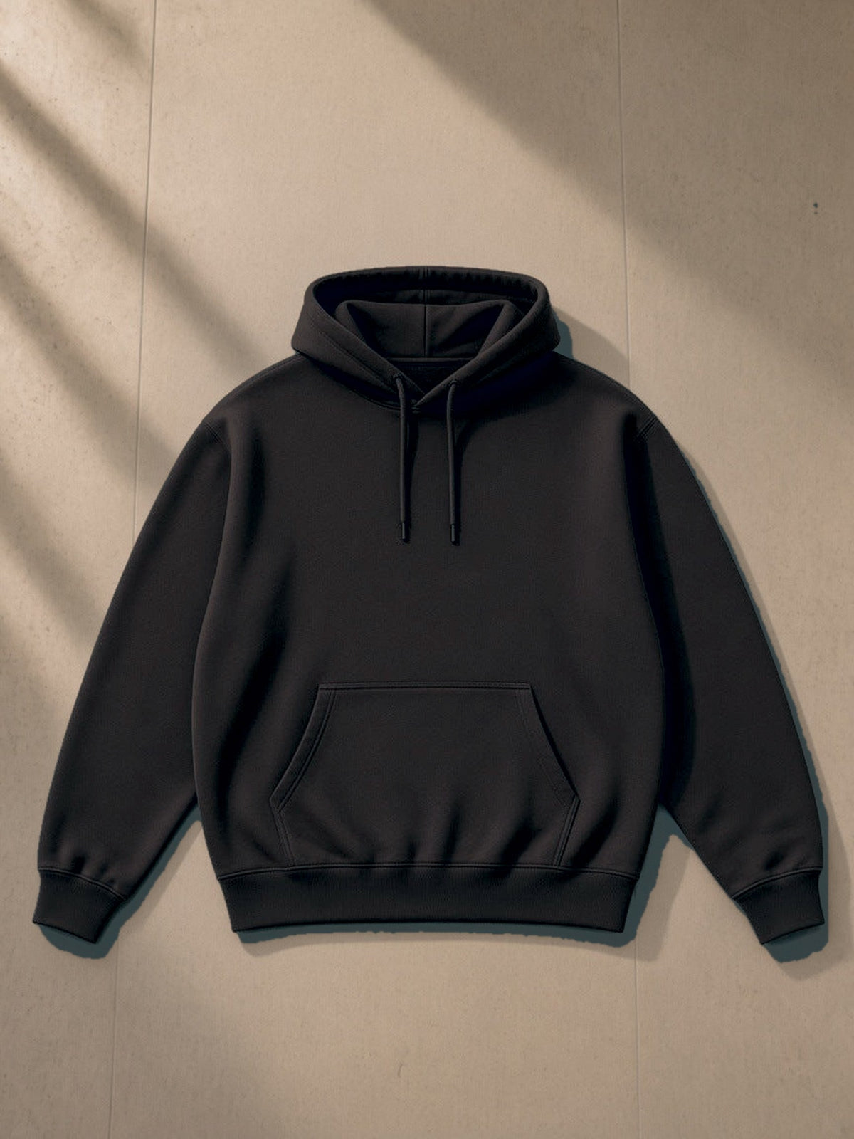 Essential Heavyweight Hoodie in Black, laid flat on pale limestone, front view