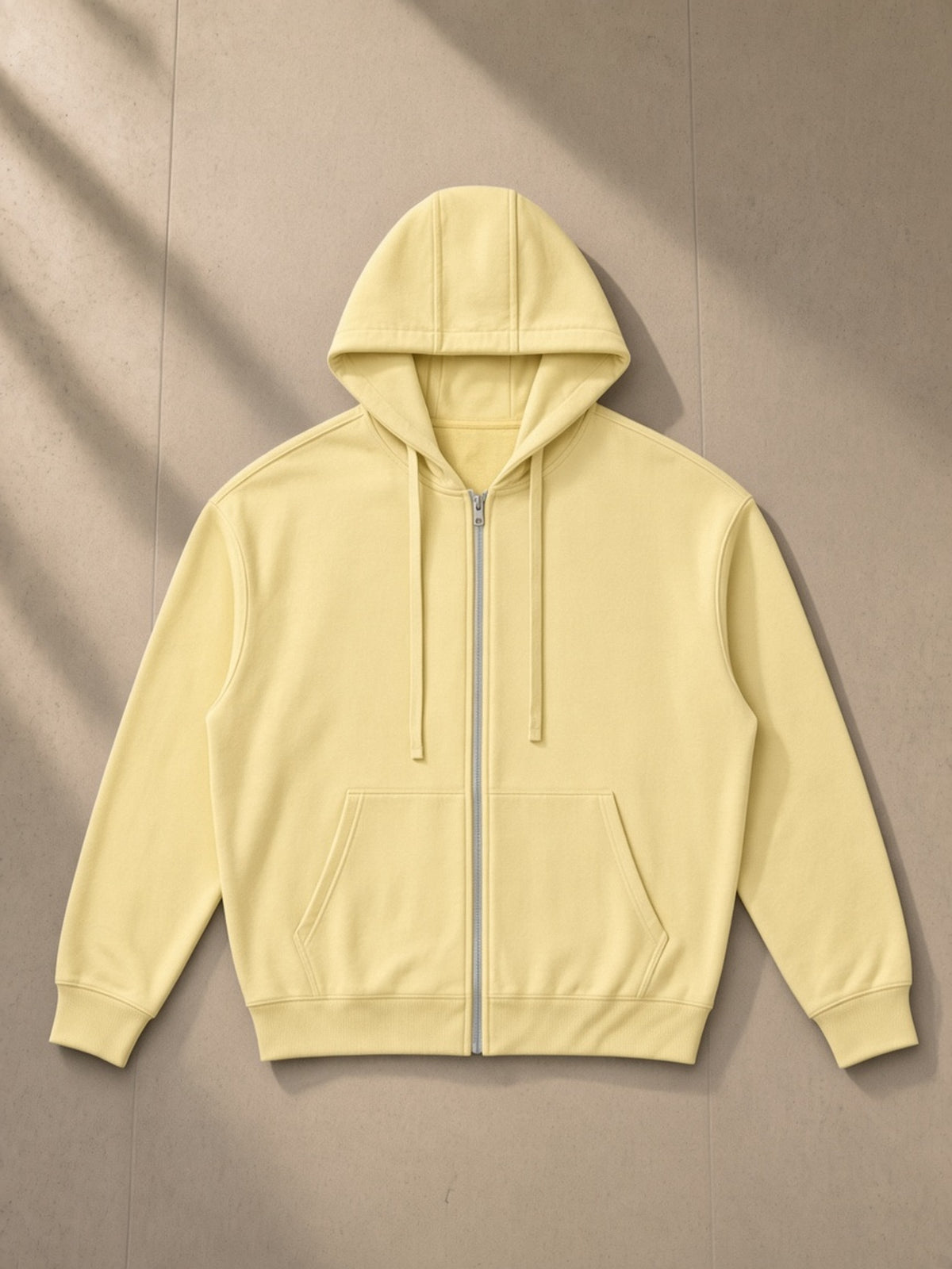 Unisex drop-shoulder zip up hoodie in Yellow, laid flat on pale limestone, front view