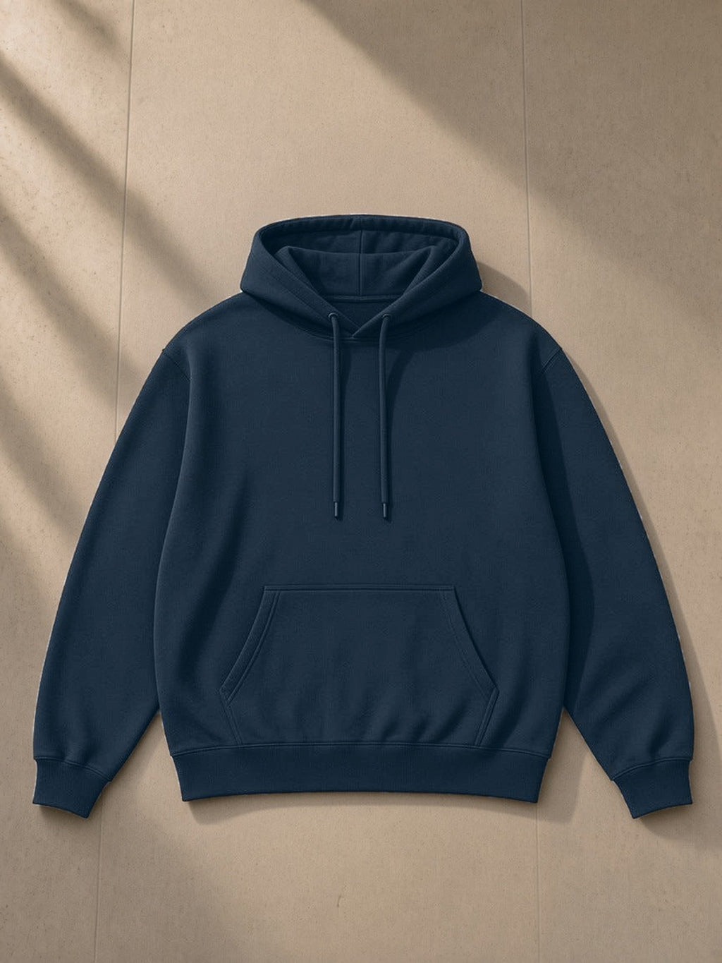 Unisex oversized drop shoulder hoodie in Navy Blue, laid flat on pale limestone, front view