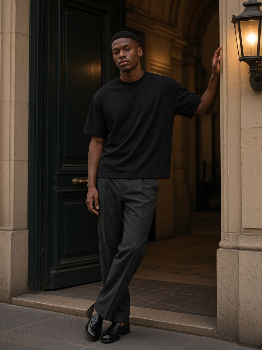 Man in the Heavyweight Boxy T-Shirt in Black standing in a stone carriage doorway in Paris at night, one hand on the frame