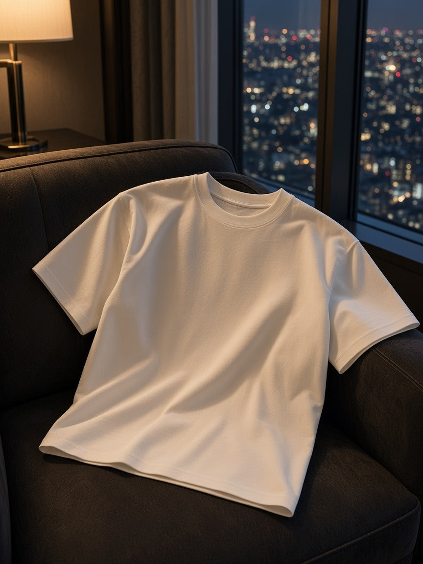 Boxy Drop Shoulder Crop T-Shirt in White tossed over a dark leather armchair in a Tokyo hotel suite at night