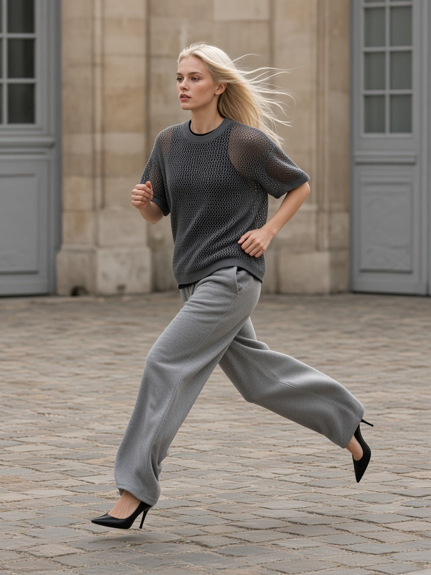 Woman in the Marcel Afters Boxy Mesh Crewneck T-Shirt in Dark Gray with grey wide trousers and heels, striding across a cobbled courtyard