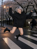 Woman in the Boxy Oversized Hoodie in Black worn as a dress with knee boots, jumping on a Nakameguro crossing in Tokyo at night