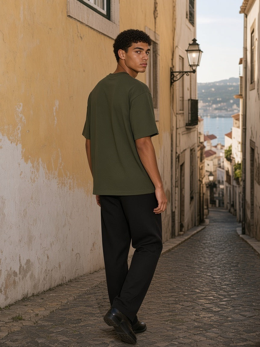 Man in the Boxy Oversized T-Shirt in Army Green walking a cobbled lane in Lisbon in the morning