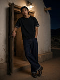 Man in the Boxy Plaid-Lined Double-Face T-Shirt in Black in the doorway of an adobe house in a New Mexico village at night