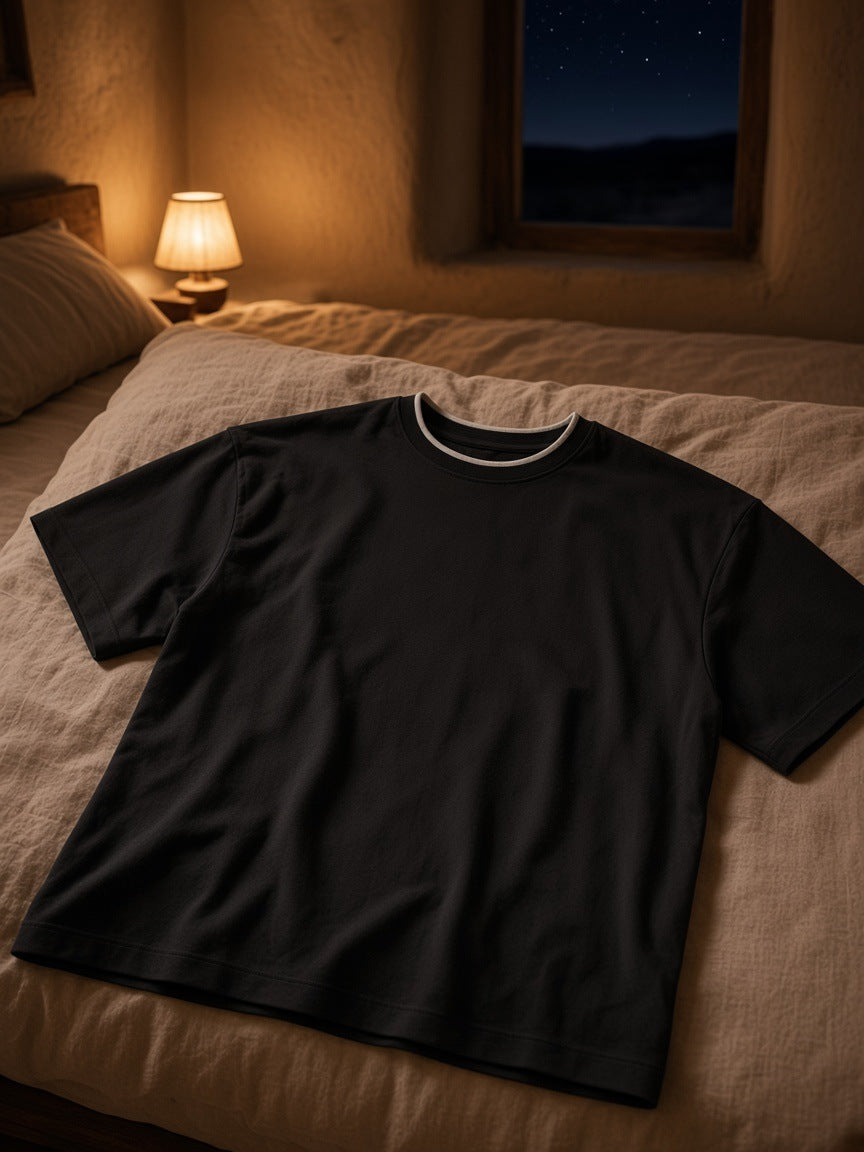 Boxy Ribbed T-Shirt in Black folded on a turned-down linen bed in a Marfa guesthouse at night