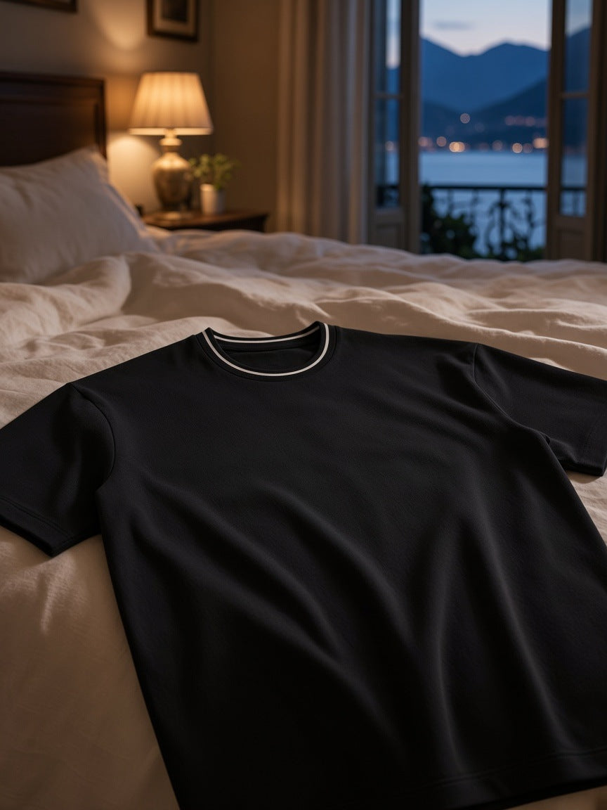 Boxy Ribbed T-Shirt in Black folded on a turned-down linen bed in a Lake Como villa at night