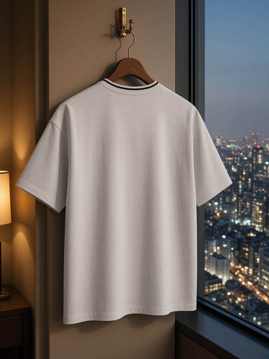Boxy Ribbed T-Shirt in Heather Gray hanging from a brass hook by the window in a Tokyo hotel suite at night