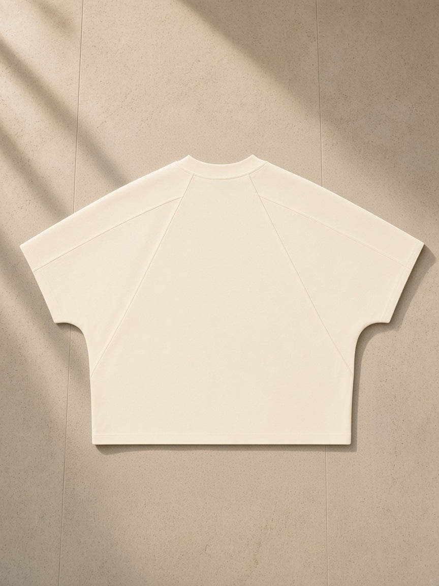 Boxy Tonal Paneling T-Shirt in Cream, laid flat on pale limestone, back view