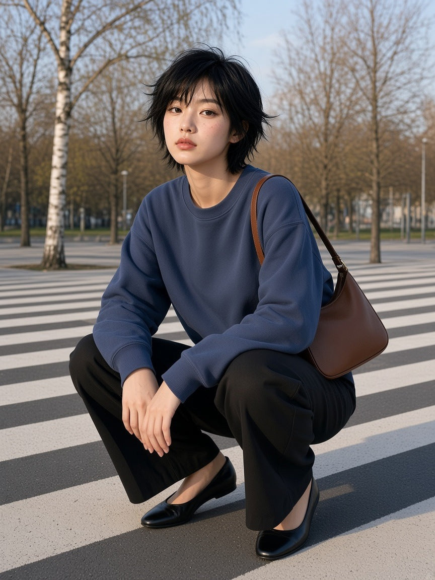 Woman in the Boxy Vintage Washed Sweatshirt in Navy Blue with wide black trousers, crouched on the striped ground of Superkilen park in Copenhagen in the morning