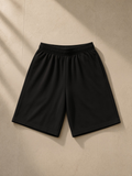 Unisex heavyweight cotton shorts in Black, laid flat on pale limestone