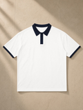 Unisex color block polo shirt in White with Navy Blue, laid flat on pale limestone