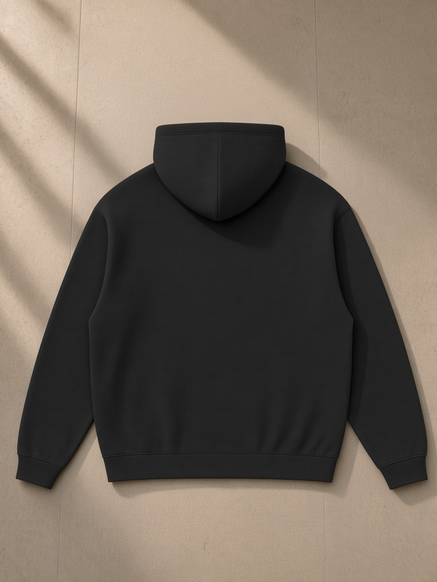 Waffle Hoodie in Black, laid flat on pale limestone, back view