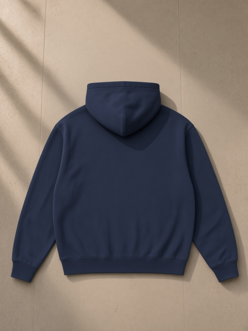 Essential heavyweight hoodie in Navy Blue, laid flat on pale limestone, back view