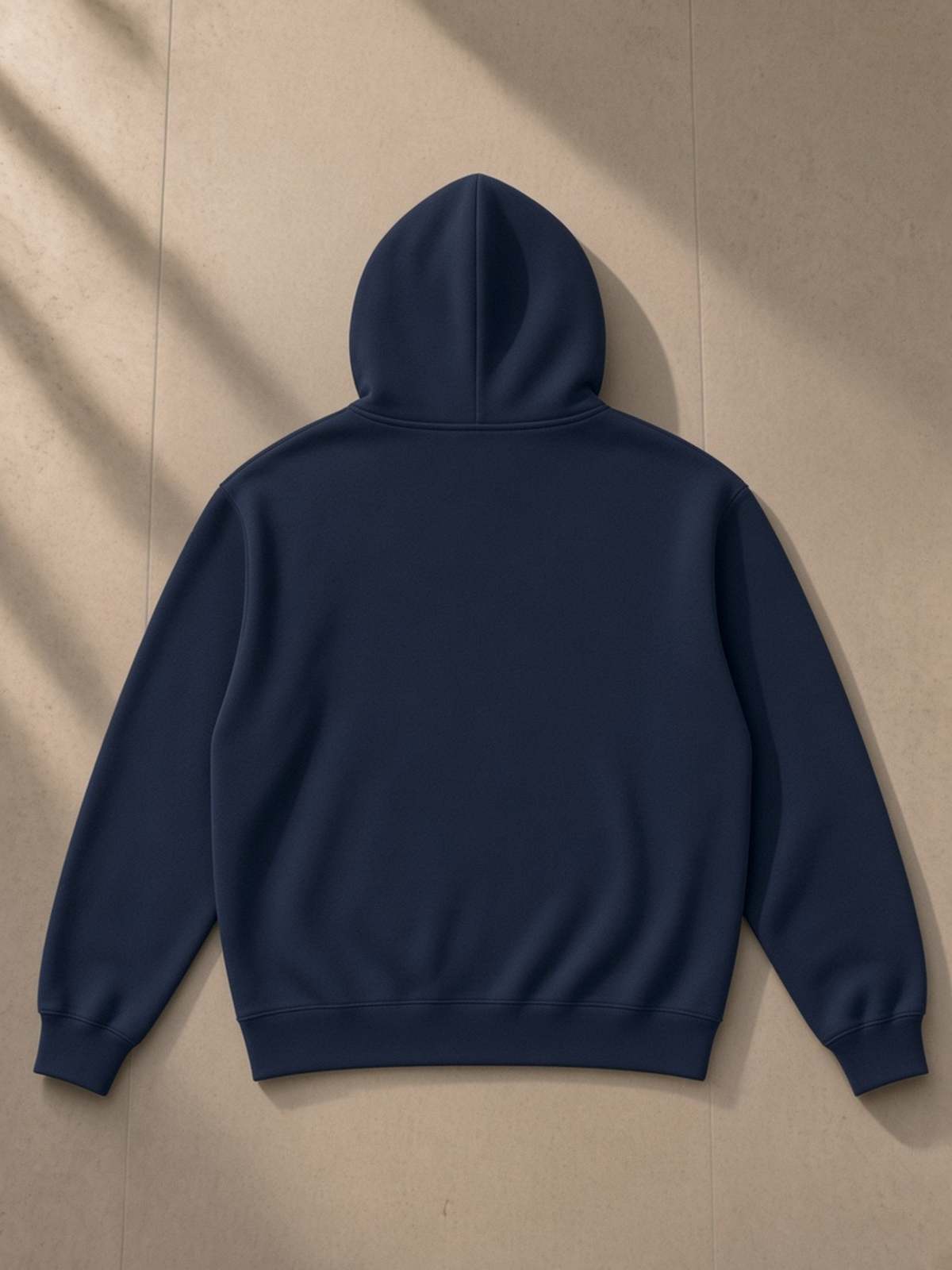 Relaxed Fit Hoodie in Navy Blue, laid flat on pale limestone, back.