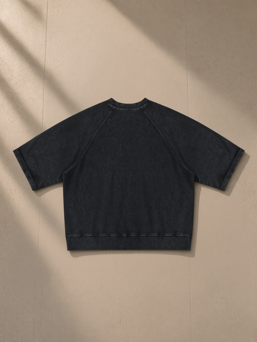 Unisex vintage wash boxy short sleeve sweatshirt in Black, laid flat on pale limestone, back view