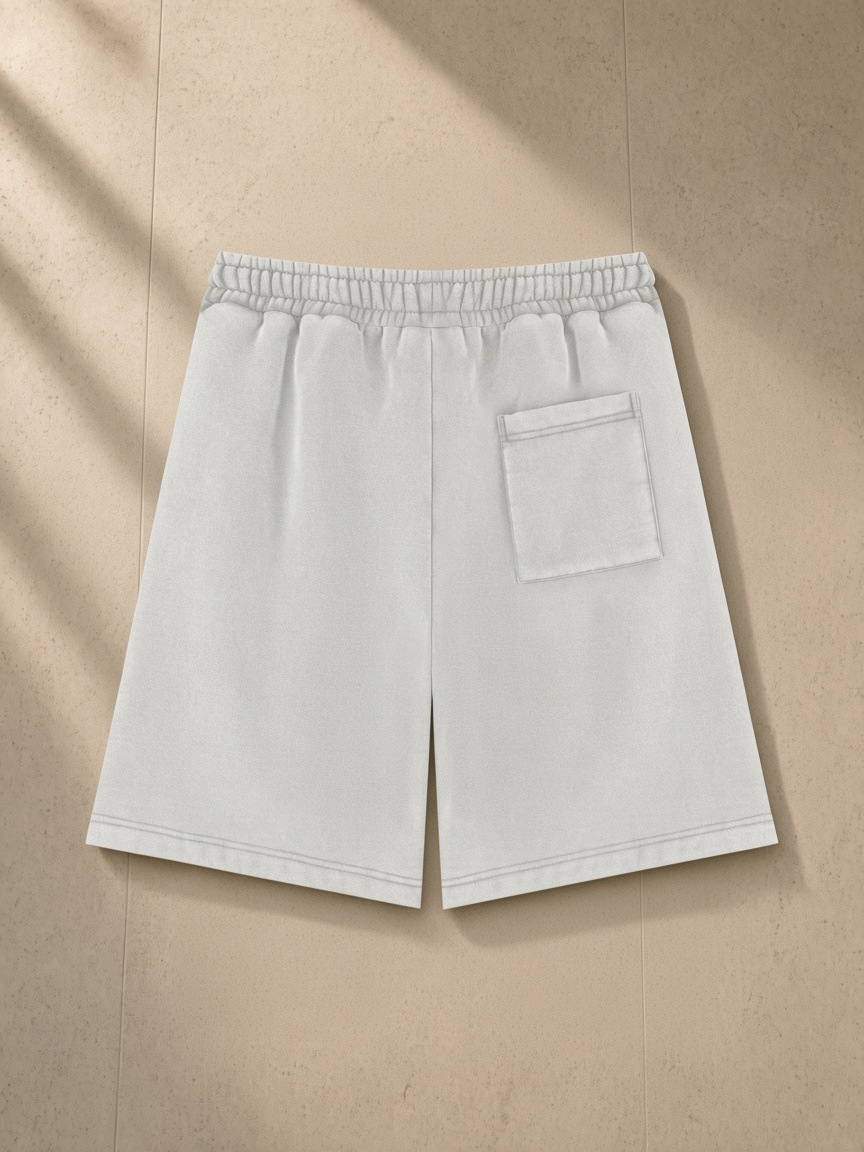 Unisex vintage wash fleece shorts in Light Gray, laid flat on pale limestone, back view