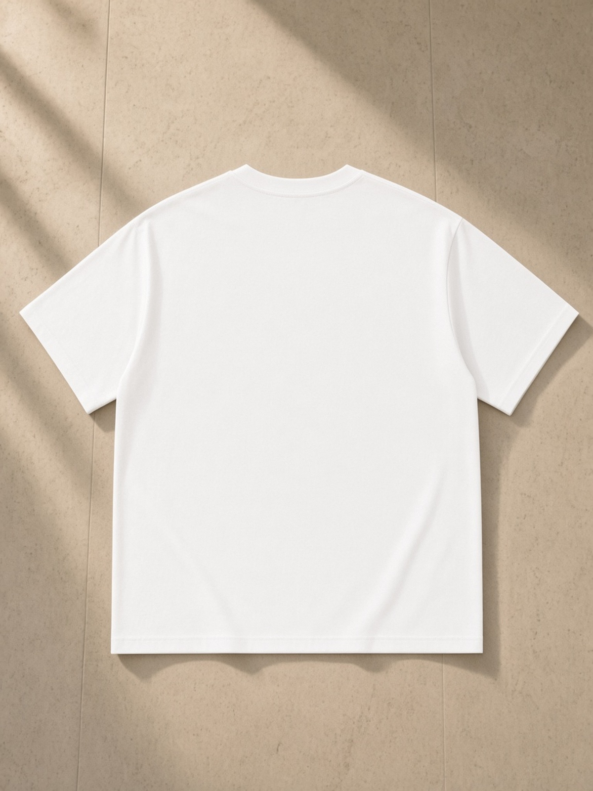 Essential Cotton T-Shirt in White, laid flat on pale limestone, back.
