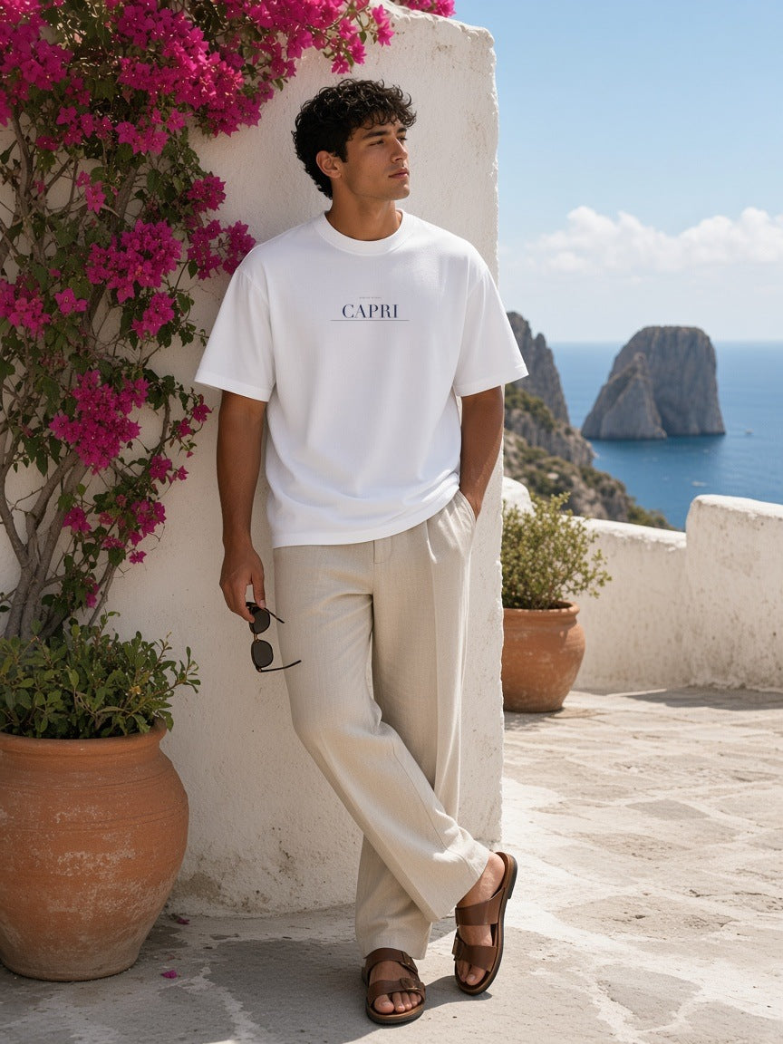 Man in the Capri Heavyweight Drop Shoulder T-Shirt in White leaning on a whitewashed wall above the sea in Capri in the morning