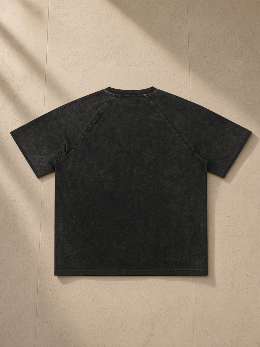 Mineral Wash Raw Edge T-Shirt in Black, laid flat on pale limestone, back.