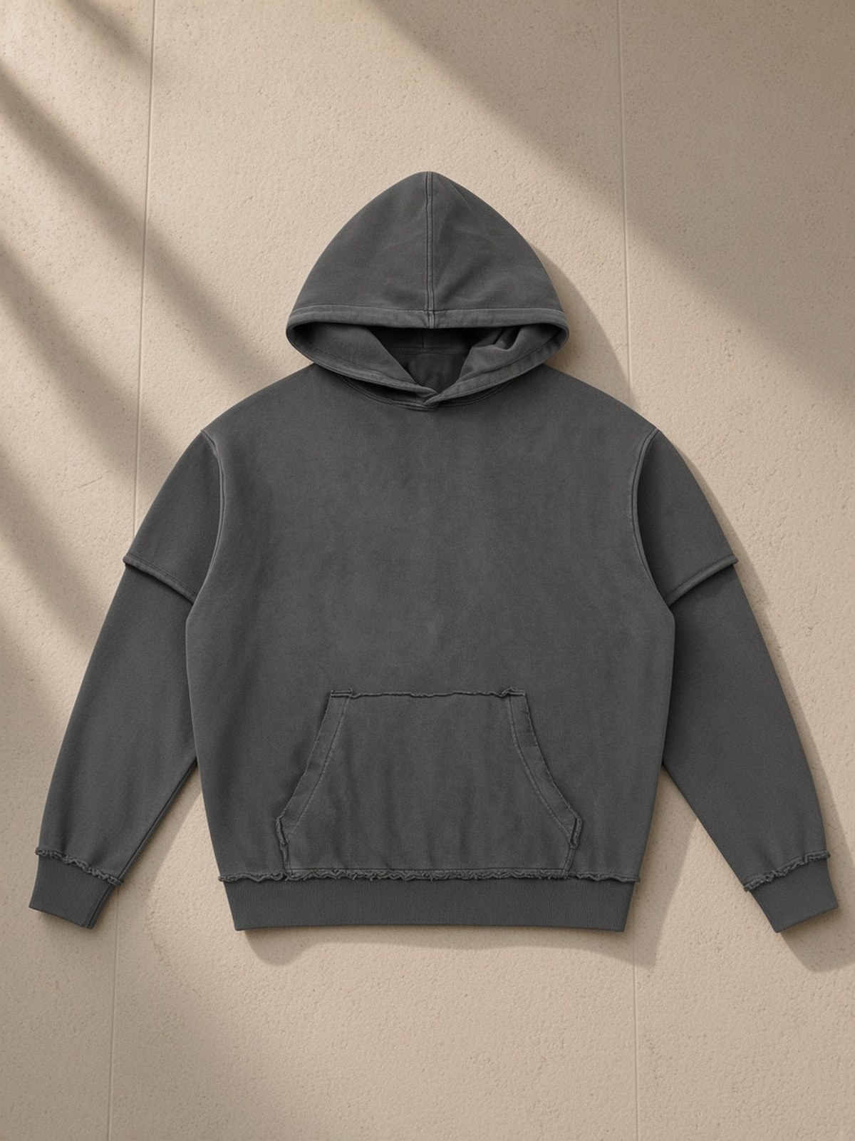 Snow Washed Raw Edge Double Layered Hoodie in Dark Gray, laid flat on pale limestone, front.